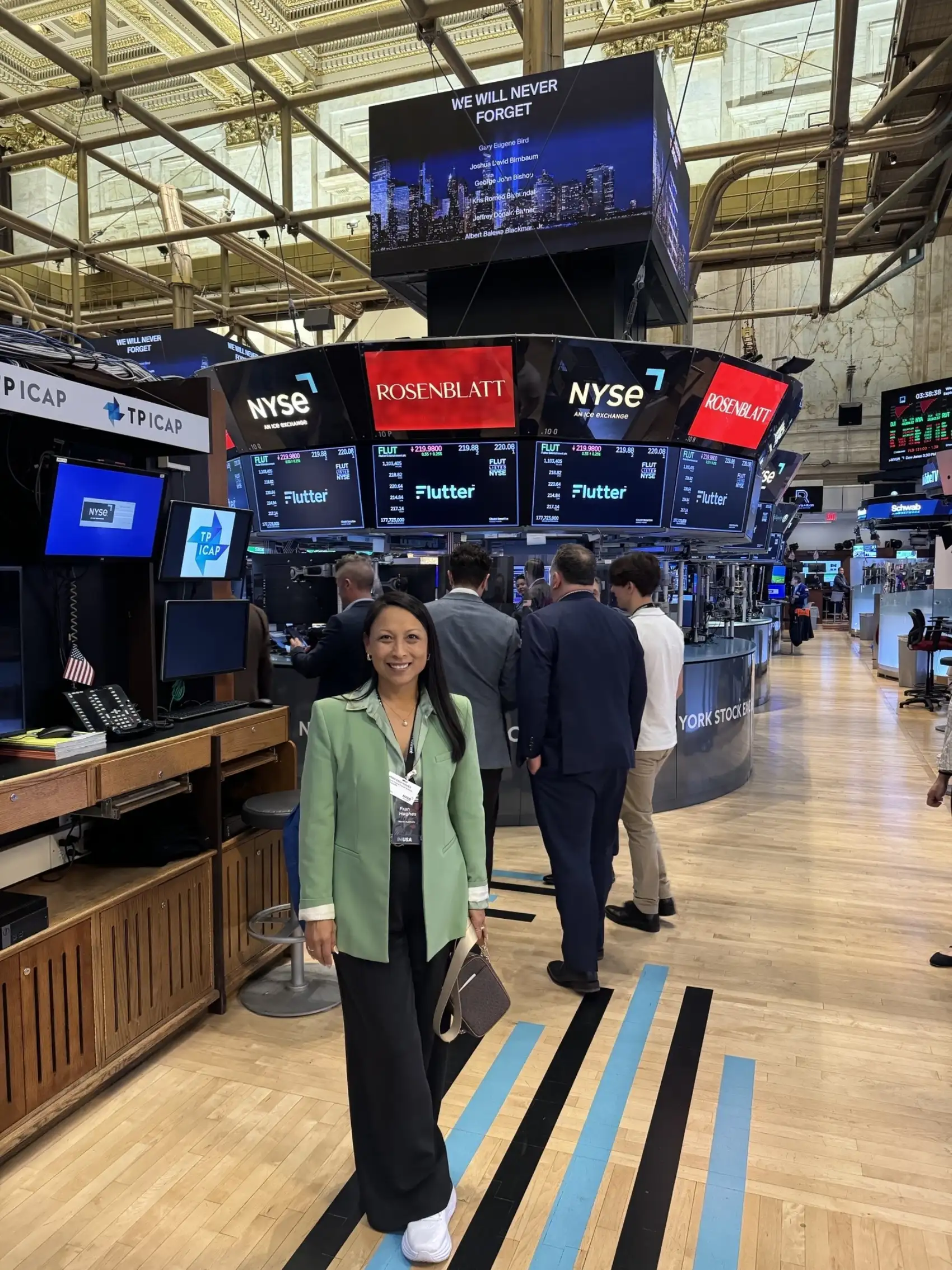 A photograph of Kate Christie smiling while standing on the trading floor of the New York Stock Exchange (NYSE).