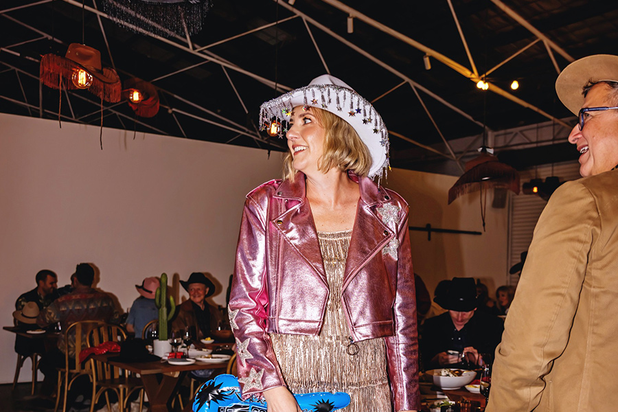 A woman in a cowboy outfit holds a guitar, representing the spirit of country music and western culture